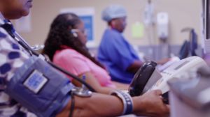 A diverse group of low-income individuals undergoing health check-ups in a modern clinic, focusing on advanced health monitoring devices and friendly healthcare providers. Include details of their blood pressure being measured in a calm environment, representing hope and care for cardiovascular health improvements.